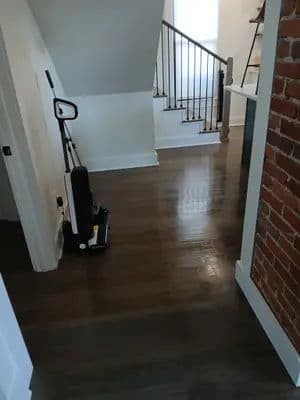 Modern hallway featuring hardwood floors, a vacuum cleaner, and a staircase.