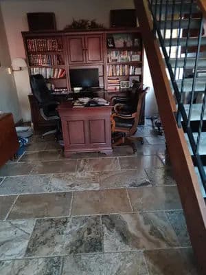 Home office with wooden desk, black chairs, bookshelves, and stone floor near staircase.
