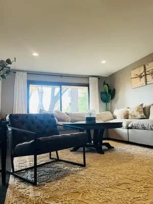 Cozy living room with a sectional sofa, tufted chair, and large window views.