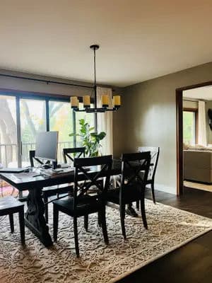 Modern dining room with a wooden table, black chairs, and large windows overlooking nature.