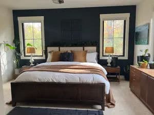 Cozy modern bedroom with dark blue walls, a large bed, and natural light from windows.