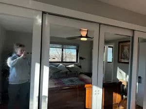 Person taking a photo in a bedroom with mirrored closet doors and large windows.