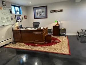 Office workspace with wooden desk, ergonomic chair, rug, and wall decor.