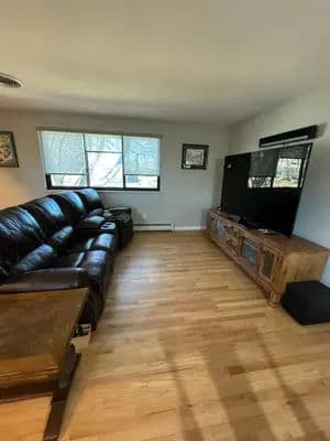 Cozy living room with leather sofa, wooden TV stand, and large flat-screen TV.