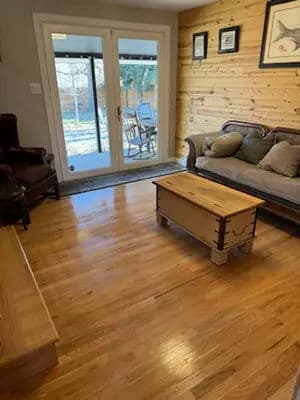 Cozy living room with wooden walls, sofa, and a coffee table overlooking outdoor greenery.