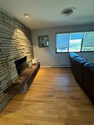 Cozy living room with stone wall, hardwood floor, and large window for natural light.