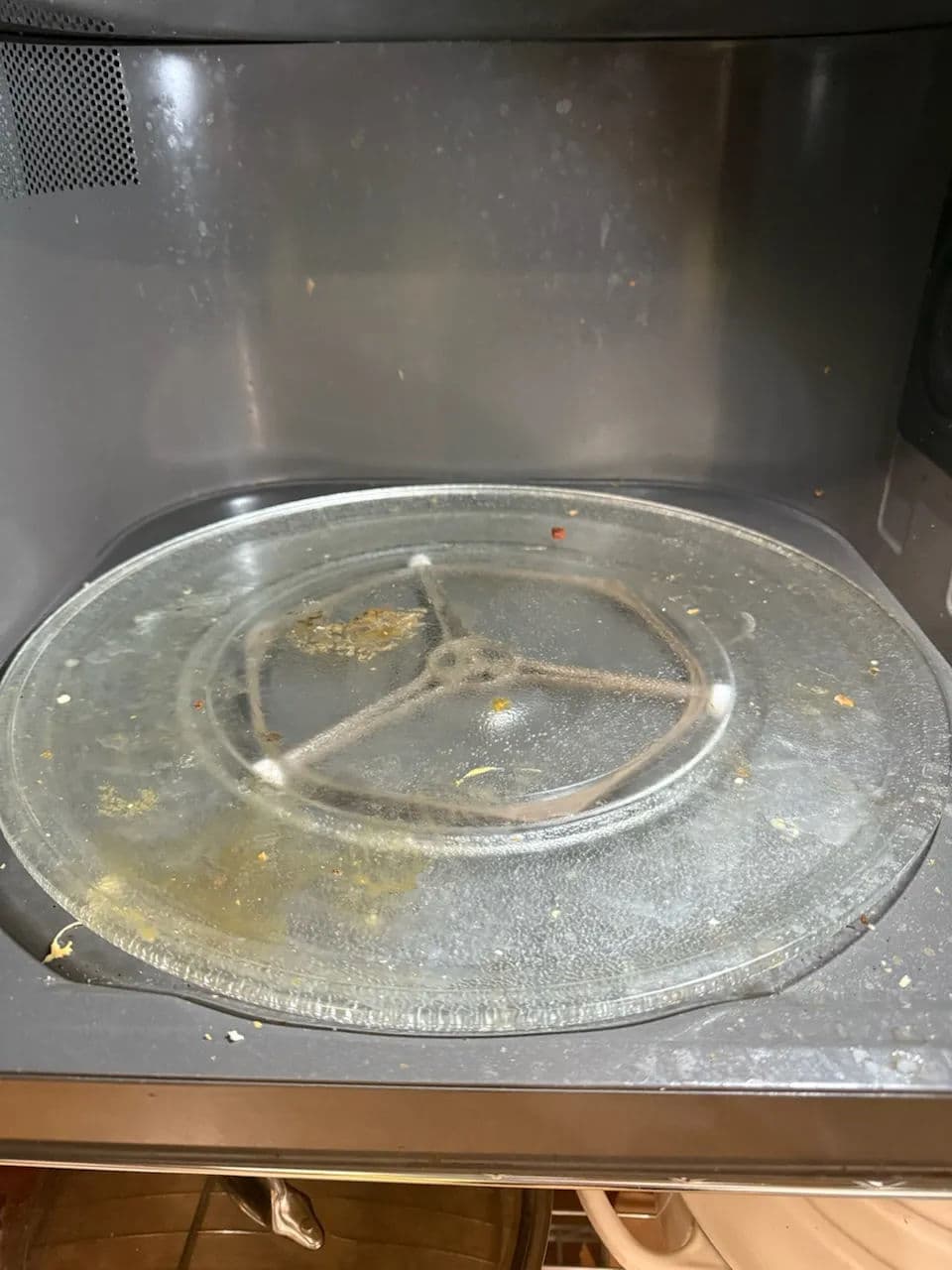 Dirty microwave turntable with food residue and grease on a gray background.