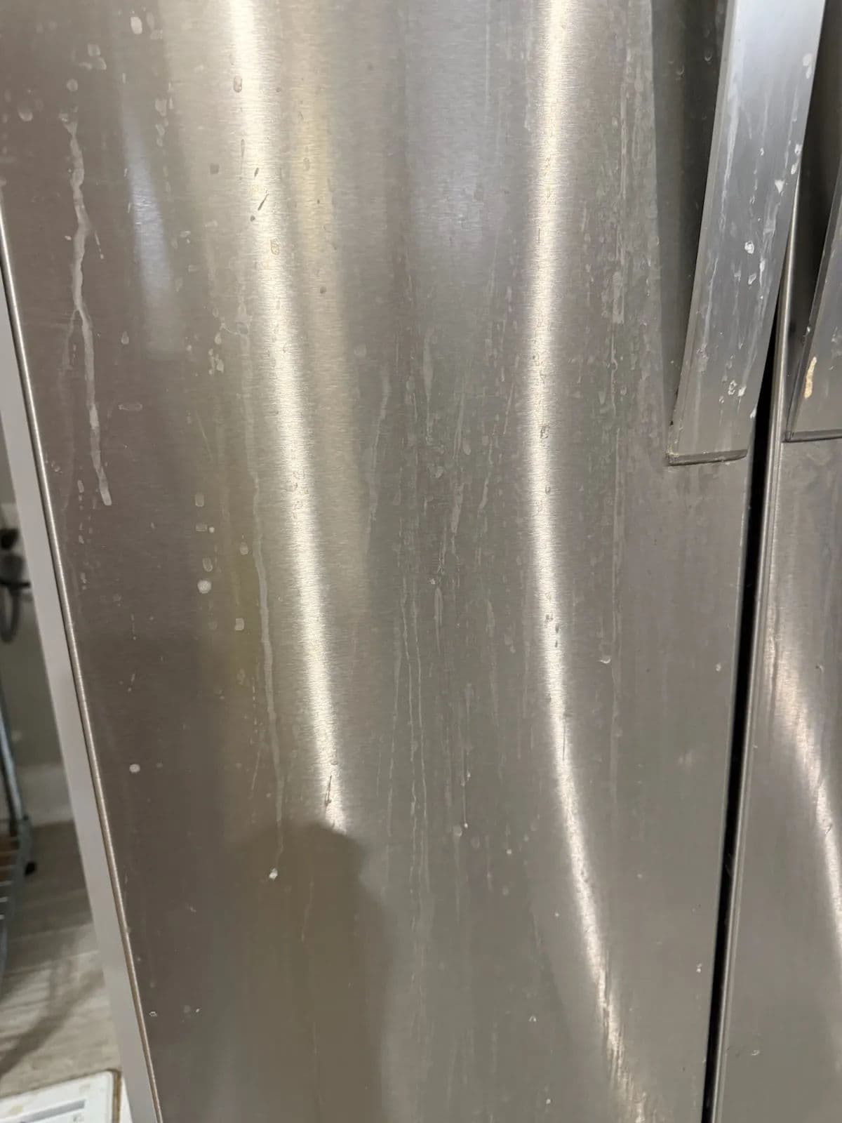 Close-up of a stainless steel refrigerator door with water stains and smudges.