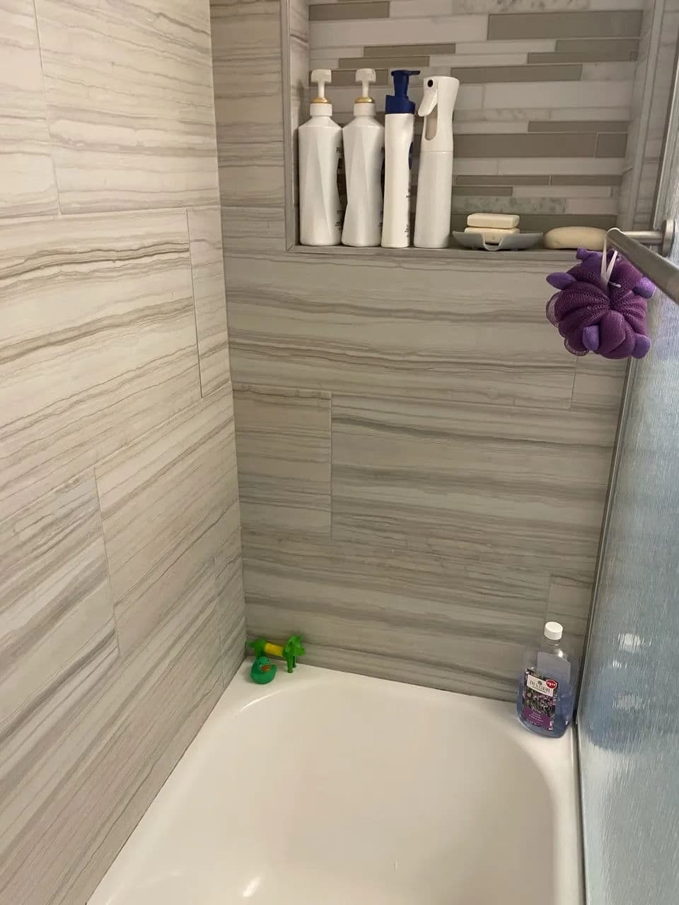 Modern walk-in shower with gray tiles, organized shampoo bottles, and colorful accessories.