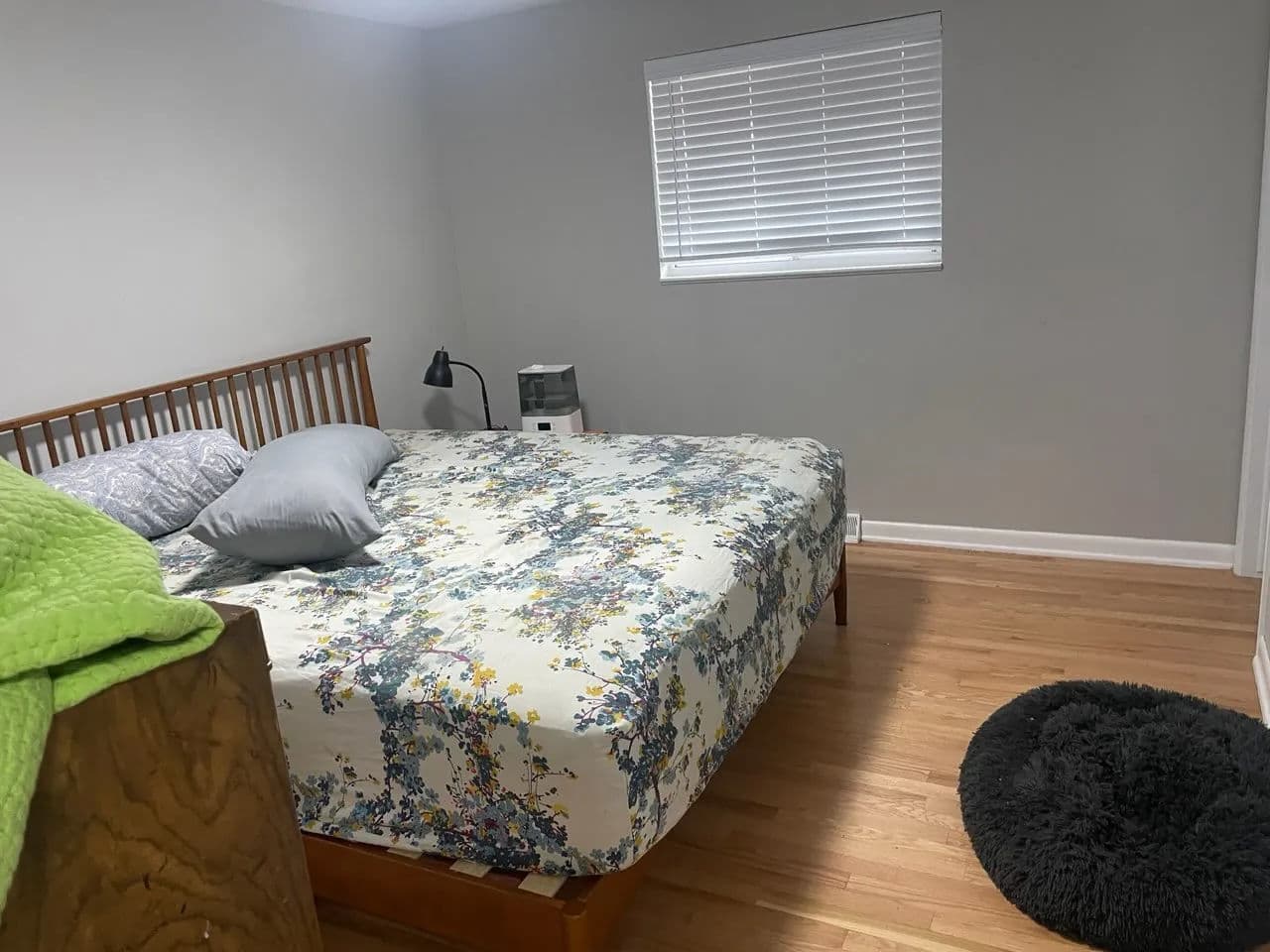 Cozy bedroom with a floral bedspread, wooden bed frame, and gray rug on hardwood floor.