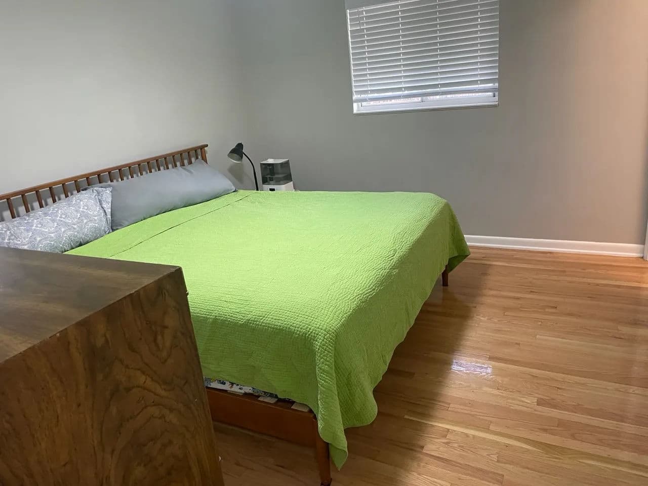 Bright bedroom featuring a green bedspread, hardwood floors, and natural light.