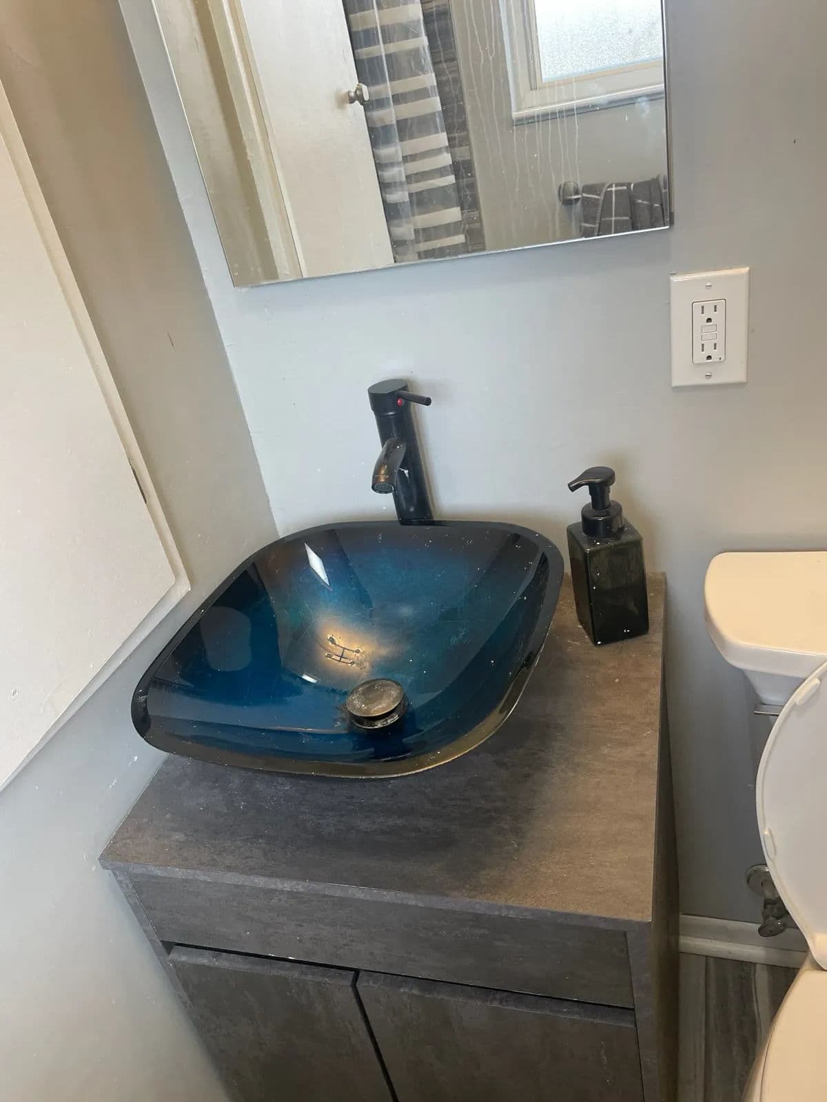 Modern bathroom sink with blue glass bowl, sleek faucet, and dark cabinetry.