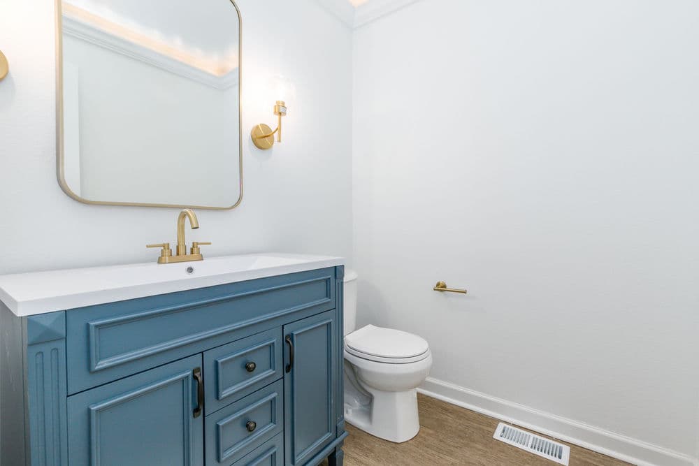 Modern bathroom with blue vanity, gold fixtures, and white walls. Clean and bright design.