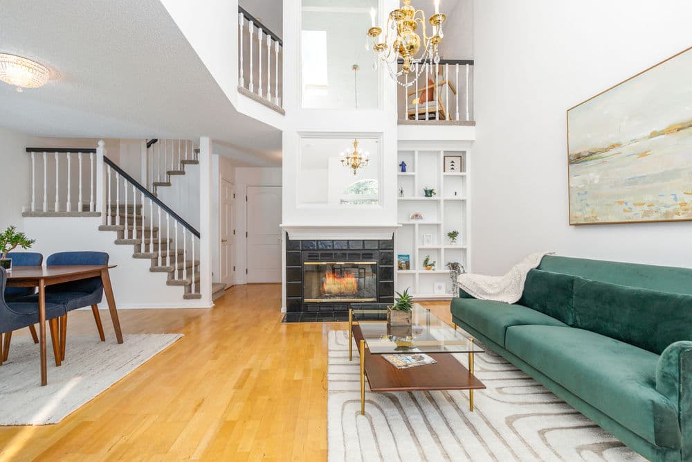 Bright living room with green sofa, fireplace, and wooden staircase in modern home interior.