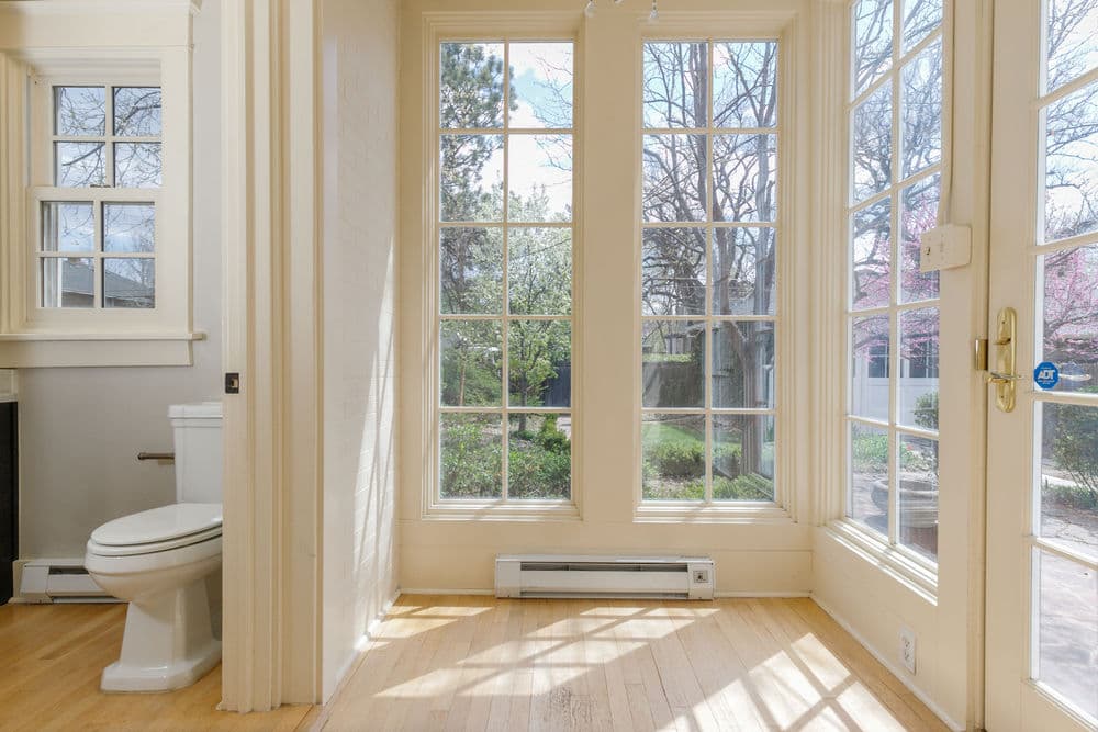 Bright interior with large windows, hardwood floors, and a white toilet in a cozy space.