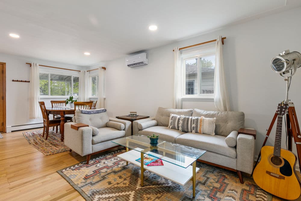 Cozy living room with light grey sofas, wooden furniture, and an acoustic guitar in a sunny space.