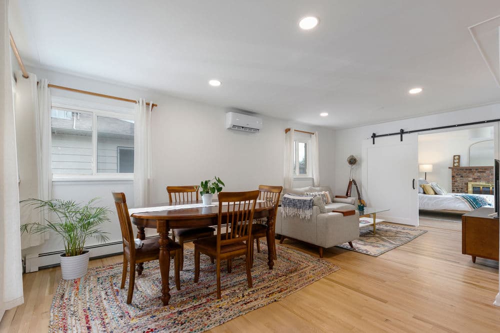 Cozy modern living space with dining area, natural light, and stylish decor. Wood flooring and plants.