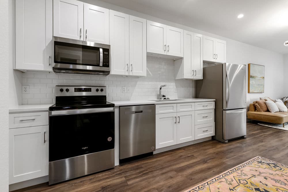 Modern kitchen with stainless steel appliances, white cabinets, and hardwood flooring.